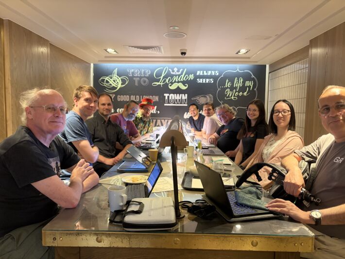 11 attendees sitting round a long table in cafe with laptops and the backdrop of a mural-style decorated wall with Trip to London Town
