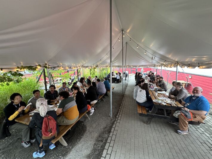 Large group of people at several tables under a large white tent.