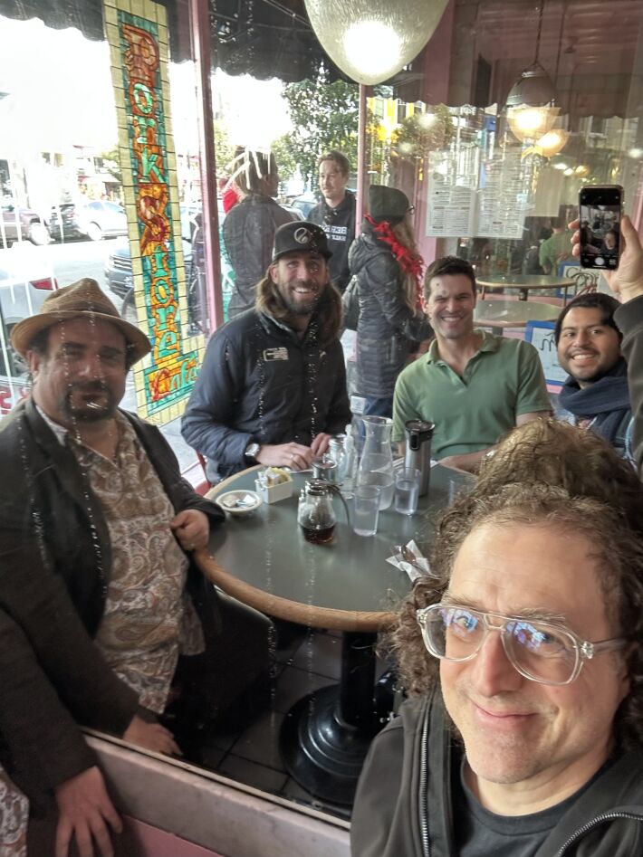 Selfie taken with four other participants in a mirror, all sitting around a round table waiting for their brunch orders.