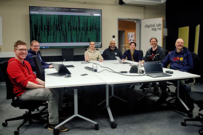 The participants of HWC Nuremberg 01/26 sitting around a table. There is a german Matrix screen (with umlauts) in the background.
